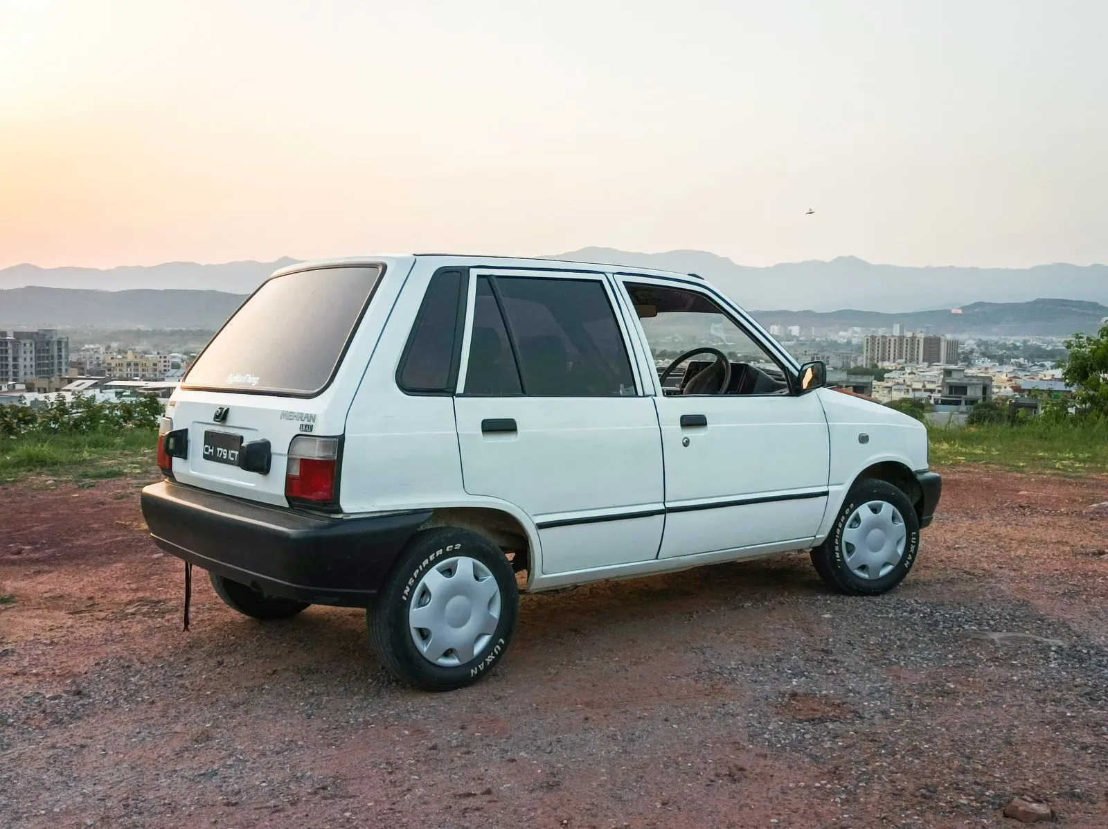 A vintage white hatchback parked on a country road at sunset, ideal for travel and transportation themes.
